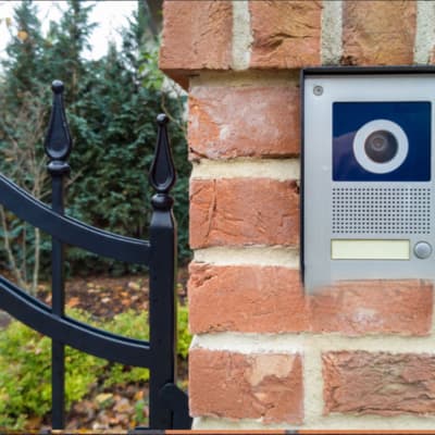 A video intercom mounted on a brick wall next to a gate